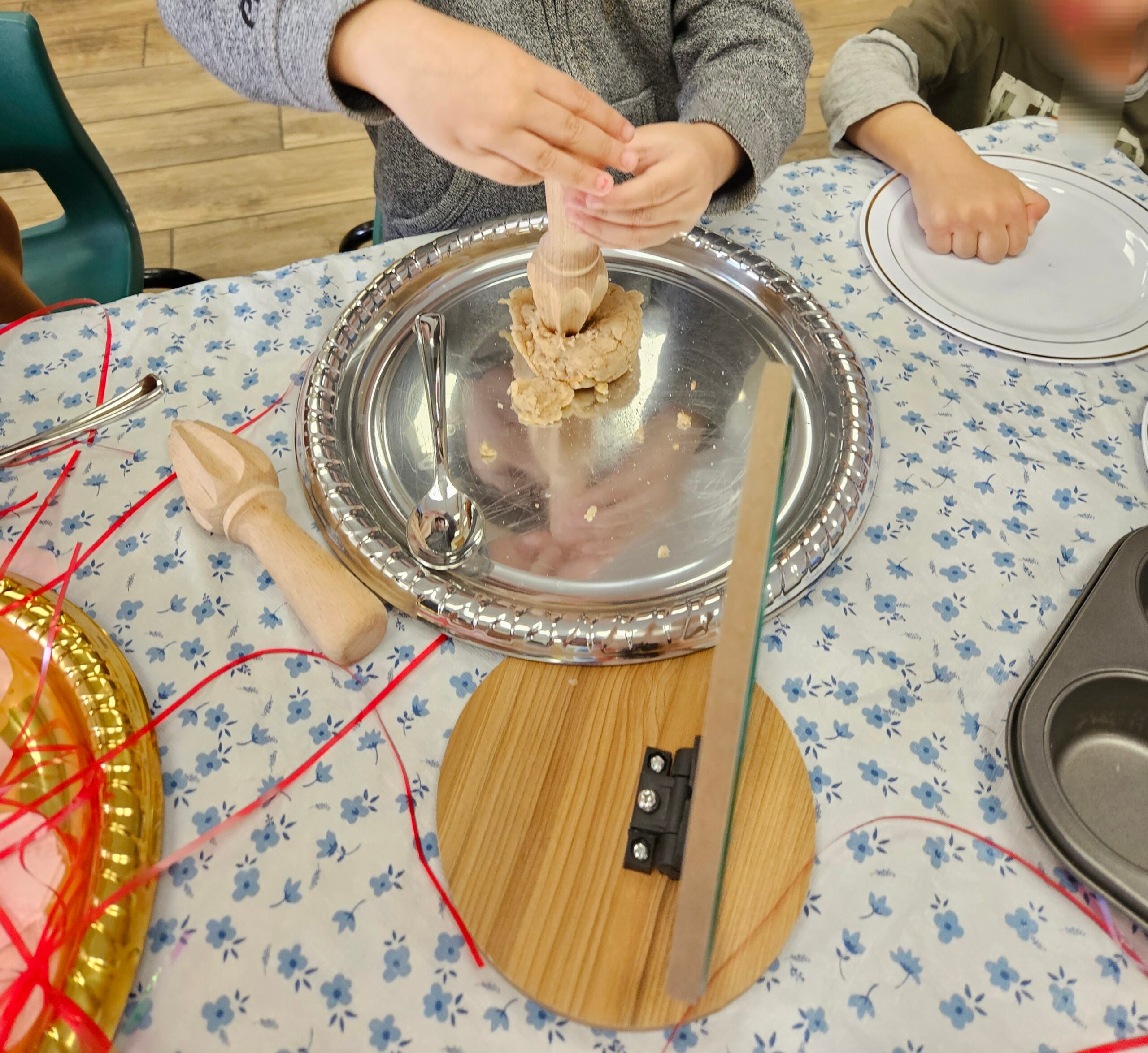 Child rolling playdough with a wooden rolling pin on a silver tray