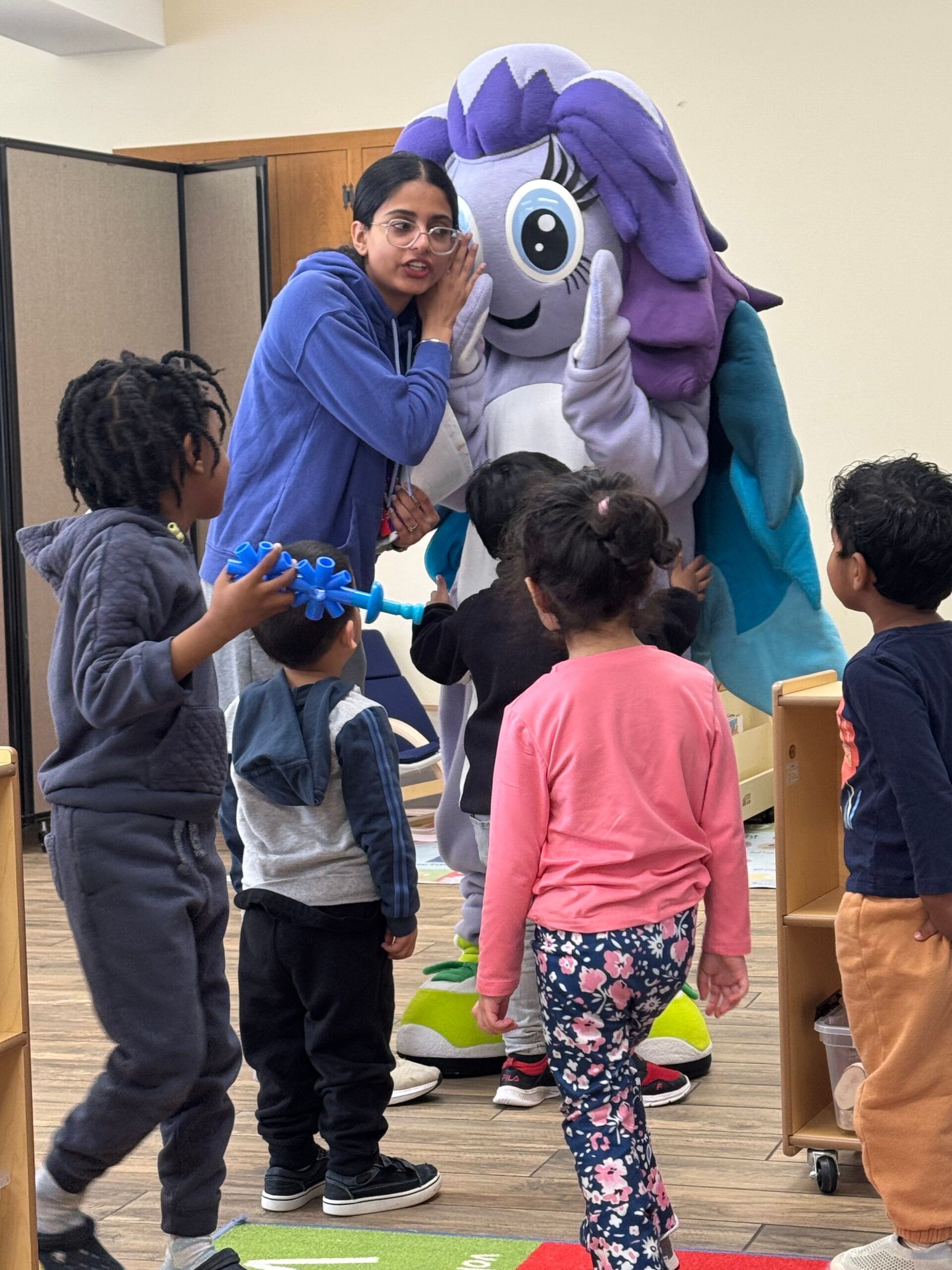 Educator and children hugging the Yuna mascot in the classroom