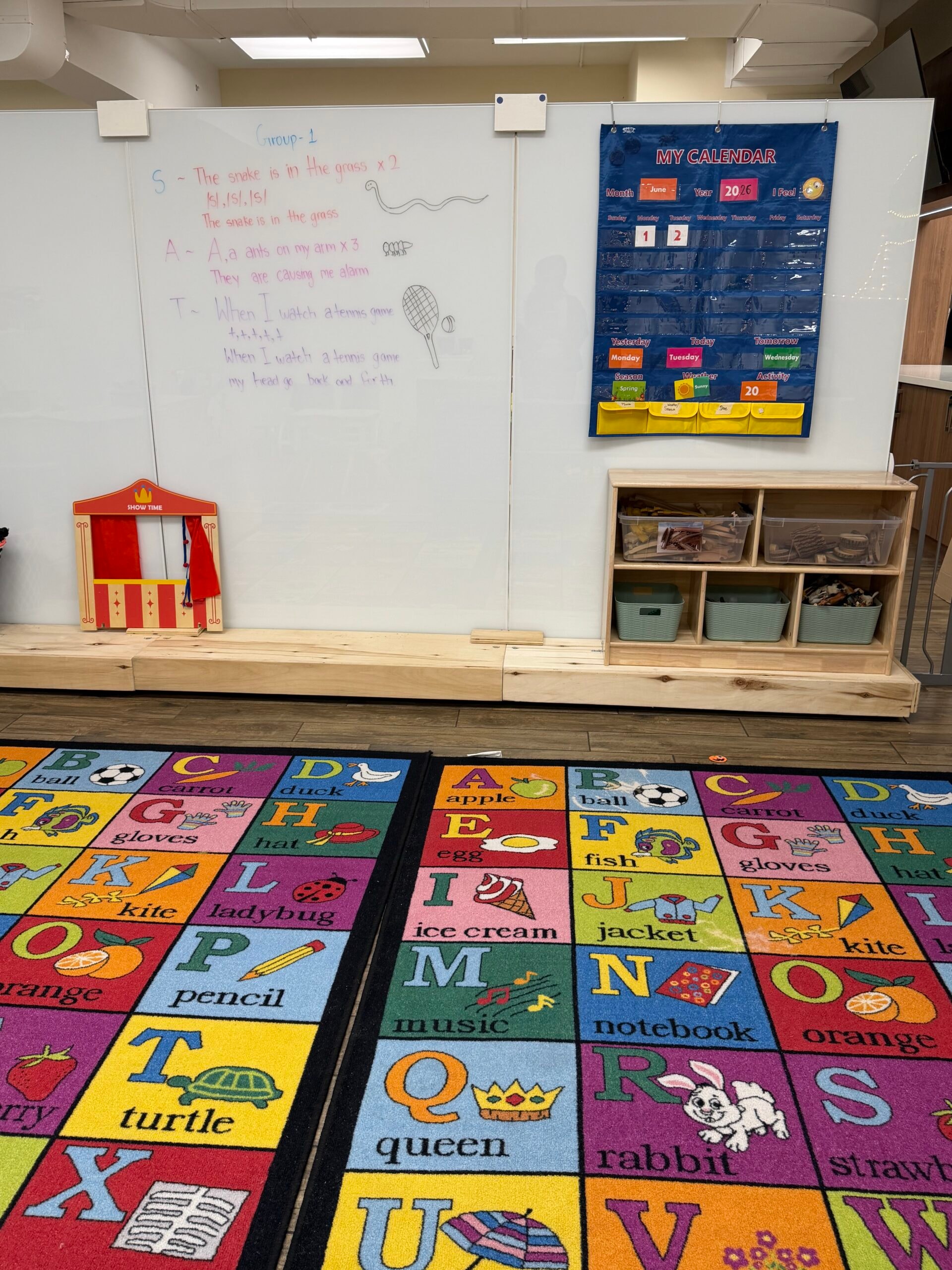 Preschool whiteboard with group lesson, calendar wall, and alphabet floor rug
